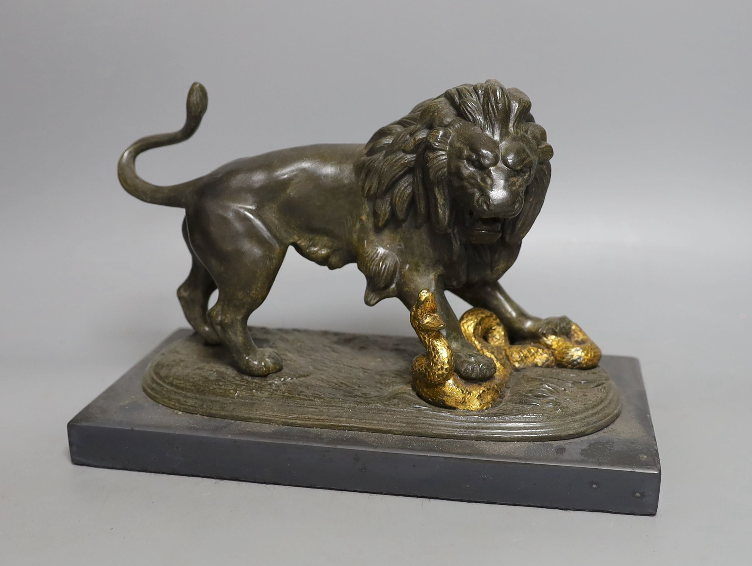 A patinated spelter figure of a lion slaying a serpent on mounted base - 24cm long